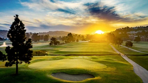 A scenic view of the golf course at Omni La Costa Resort & Spa, featuring well-manicured greens, sand bunkers, and a backdrop of lush trees and rolling hills.